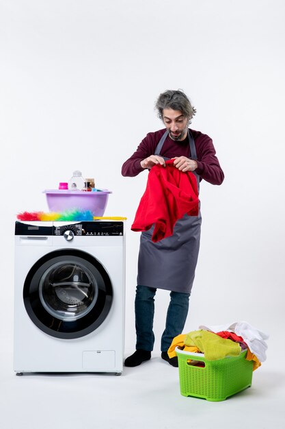 Вид спереди экономка, держащая мытье, стоя возле стиральной машины на белом фоне