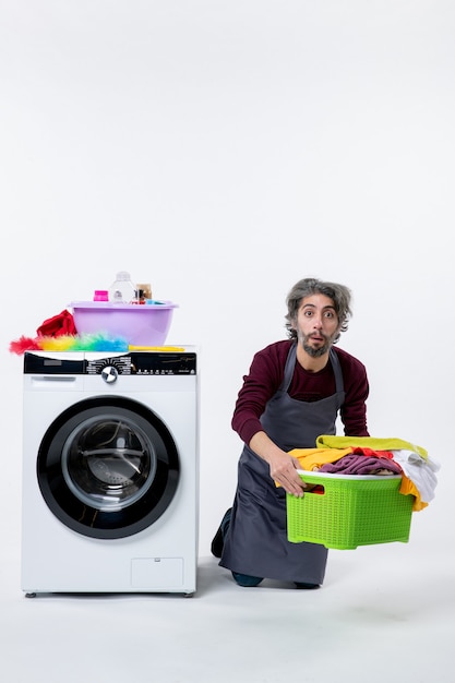 Front view housekeeper man kneeing near washer holding laundry basket on white background