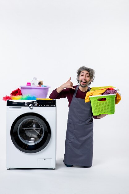 Front view housekeeper man making call me phone sign holding laundry basket on white background