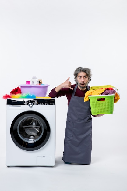 Front view housekeeper man making call me sign holding up laundry basket on white background