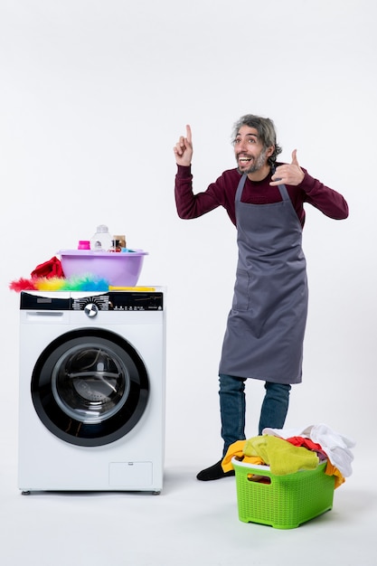 Front view housekeeper man making call me sign standing near washer laundry basket on white background