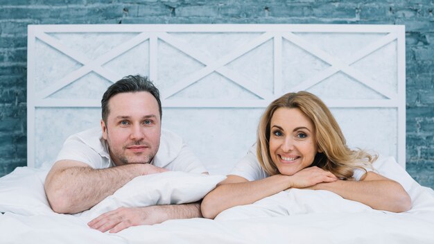 Front view of husband and wife lying on white bed looking at camera