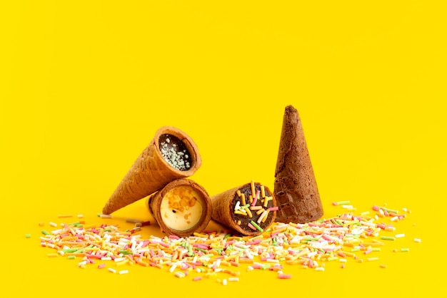 A front view ice-cream horns along with multicolored candy particles on yellow, candy sweet sugar color