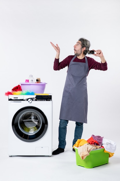 Front view interested man holding card standing near washing machine on white background