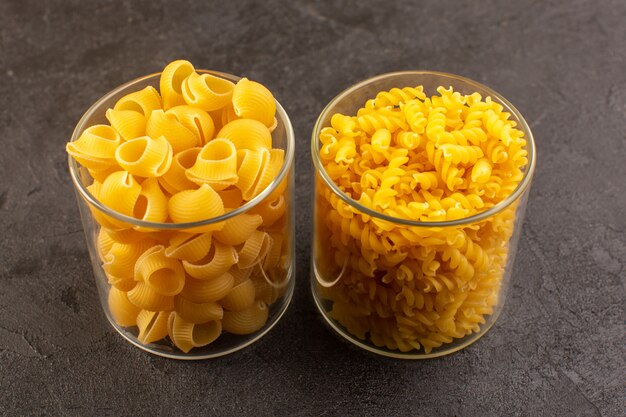 A front view italian dry pasta yellow raw inside plastic bowl isolated on the dark