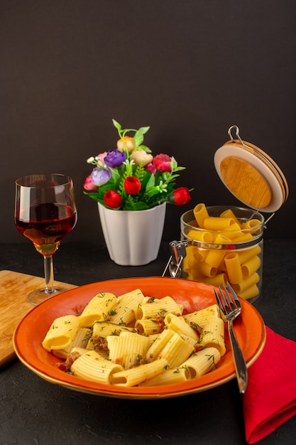Una pasta italiana di vista frontale cucinata gustosa salata all'interno di un piatto rotondo arancione con fiori all'interno tuffo sul tappeto progettato e sulla scrivania scura