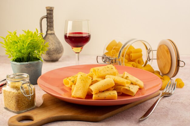 A front view italian pasta tasty meal inside pink plate along with flower and raw pasta on pink