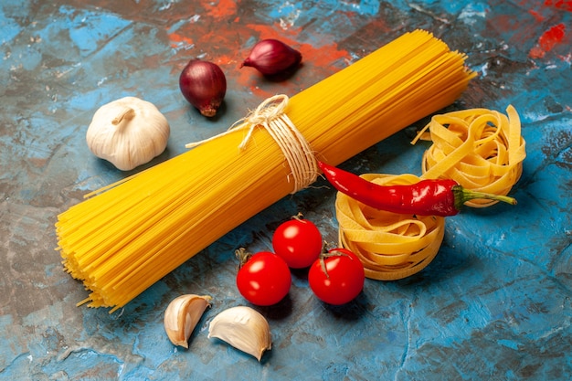 Front view of Italian various pastas for dinner preparation garlics peppers tomatoes onions on blue background