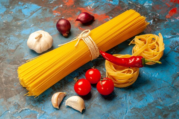 夕食の準備のためのイタリアの様々なパスタの正面図青背景にニンニクピーマントマト玉ねぎ