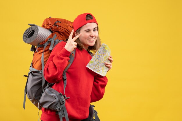 Front view joyful female backpacker holding travel map making victory sign