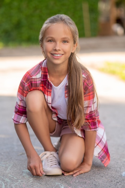 Front view of a joyful girl with a piece of colored chalk in her hand looking ahead