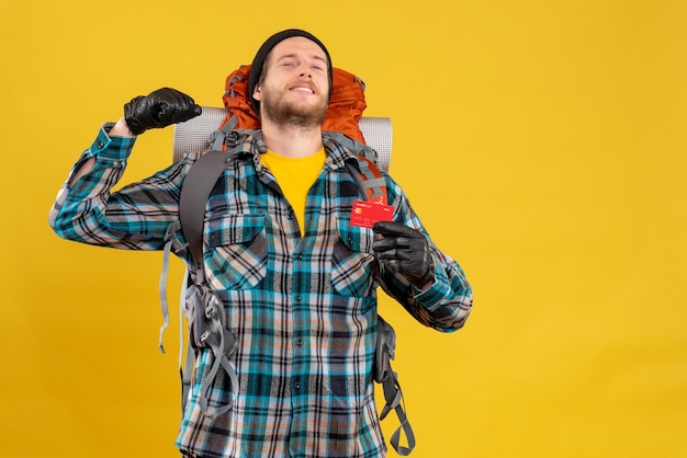 Front view of joyful young backpacker with black hat holding discount card