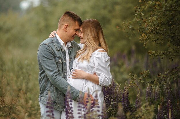 赤ちゃんを期待しているちょうど結婚した白人カップルの正面図、ルピナスの花で牧草地でほとんどキスしている