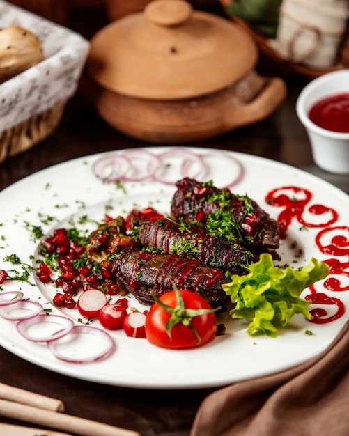 Front view khan kebab with tomato onion and pomegranate with herbs on a plate