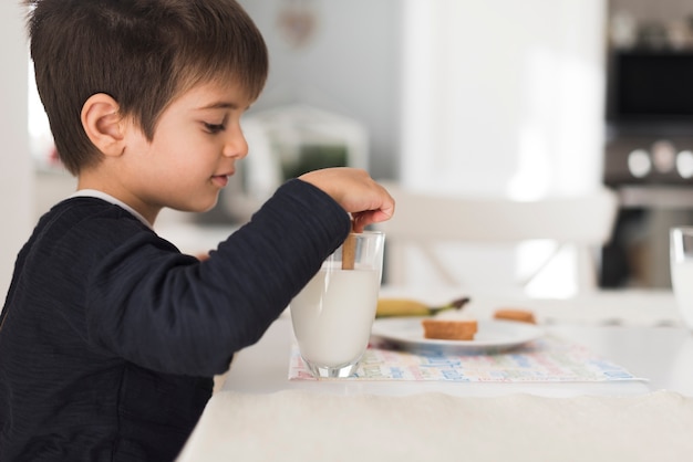 Front view kid dipping biscuit in milk