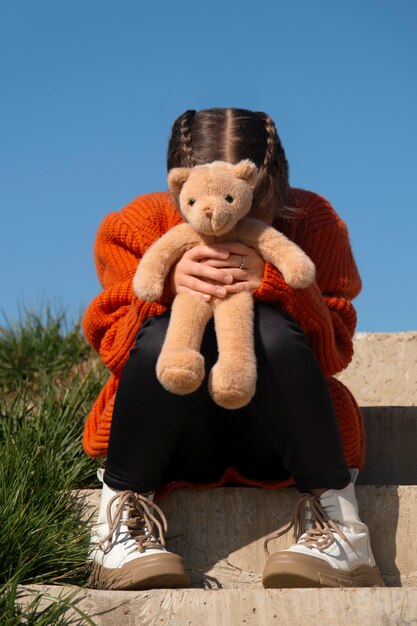 Front view kid holding teddy bear outdoors