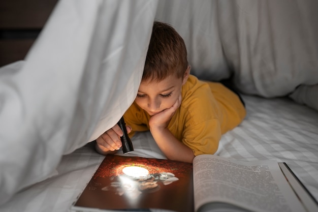 Free photo front view kid reading magazine with flashlight