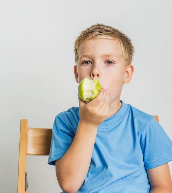 Front view kid with blonde hair bitting an apple