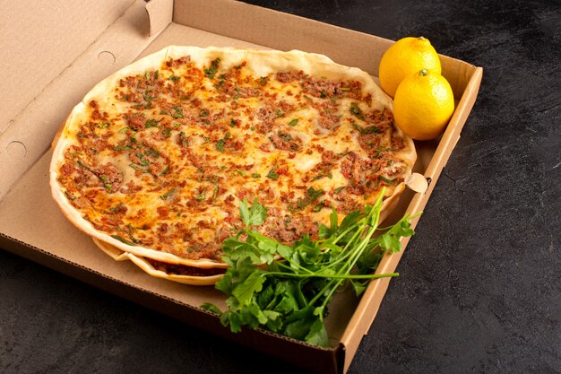 A front view lahmacun dough with minced meat along with greens and lemon inside paper box tasty pastry meal