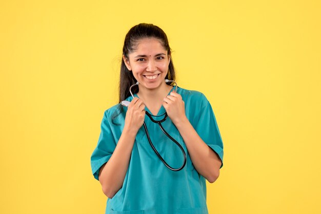 Front view laughing female doctor holding stethoscope in her hands standing on yellow background