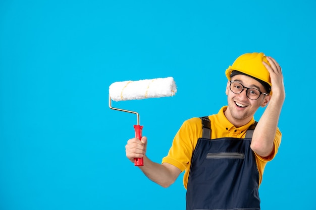 Front view laughing male builder in uniform and helmet on blue 