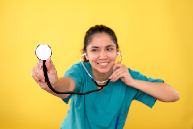 黄色の背景に聴診器を保持している制服を着た女性医師を笑っている正面図