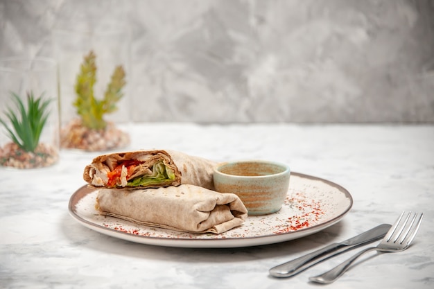 Front view of lavash wrap and yogurt in a small bowl on a plate and cutlery set on stained white surface