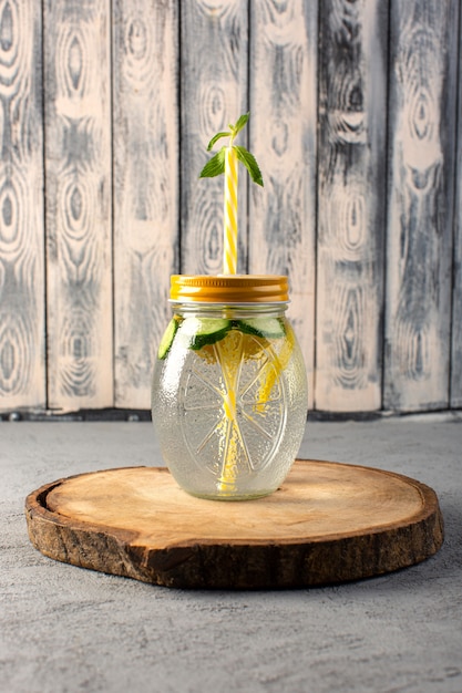 Free photo a front view lemon cocktail fresh cool drink inside glass cup sliced lemons straw on the wooden desk and grey background cocktail drink fruit