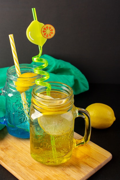 Вид спереди лимонный коктейль свежий прохладный напиток внутри нарезанные стеклянные чашки и целые лимоны красочные соломинки на темном фоне фруктовый напиток коктейль
