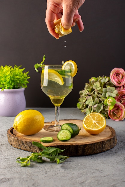 A front view lemon cocktail fresh cool drink inside glass getting some lemon juice sliced lemons straw on the wooden desk and grey background cocktail drink fruit