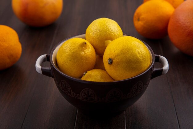 Front view lemons in a bowl with oranges and grapefruits on a wooden background