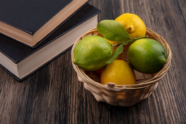 Лимоны с лаймом в корзине и книги на деревянном фоне, вид спереди