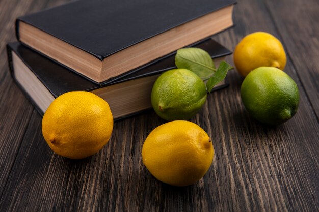 Limoni di vista frontale con limette e libri su fondo di legno