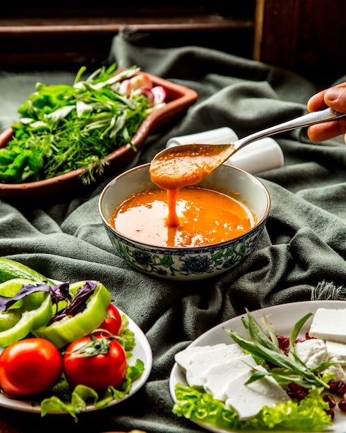 Free photo front view lentil soup traditional azerbaijani soup with a spoon over a plate in hand and with greens vegetables and cheese on the table