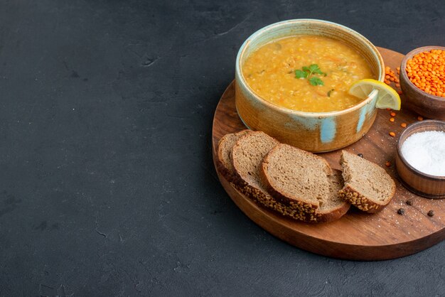 Суп из чечевицы, вид спереди с соленой сырой чечевицей и темными буханками хлеба на темной поверхности