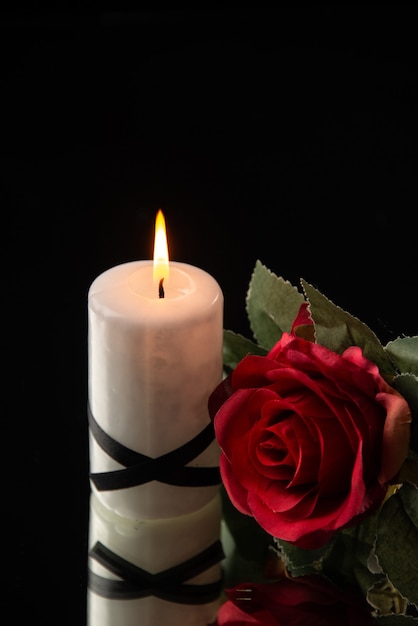 Front view of lighting candle with red flower on black