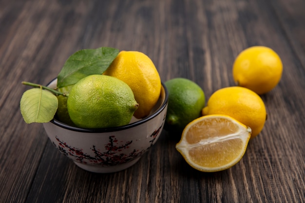 Foto gratuita vista frontale limette con limoni in una ciotola su sfondo di legno