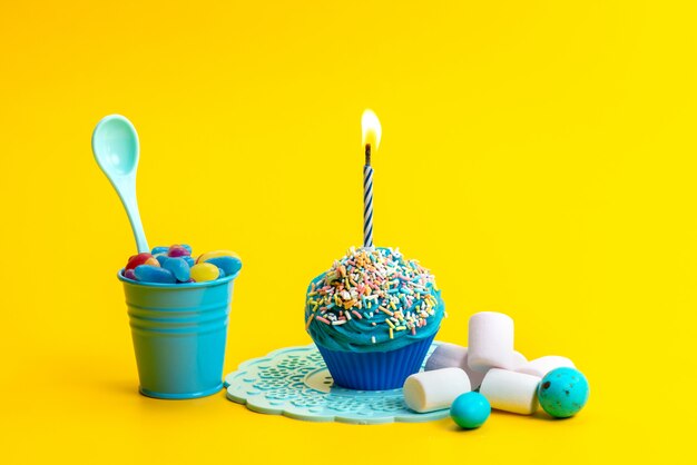 A front view little birthday cake blue colored with marshmallows and candies on the yellow desk cake biscuit  color