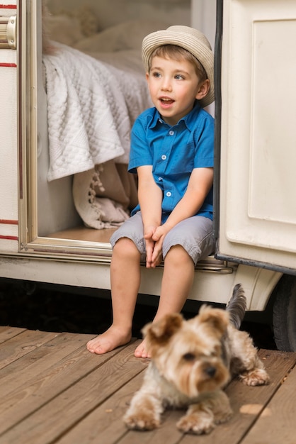 Free photo front view little boy sitting on a caravan next to a cute dog