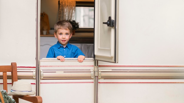 Front view little boy standing in front of a caravan's door