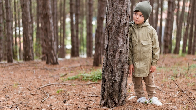 Free photo front view little boy standing next to a tree with copy space