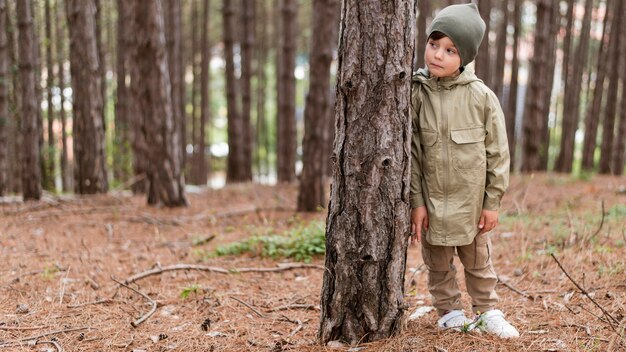 Front view little boy standing next to a tree with copy space