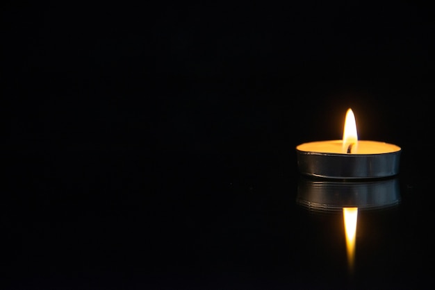 Front view of little burning candle on black