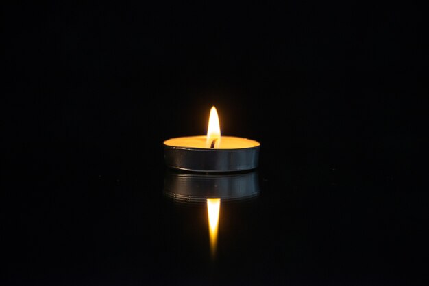 Front view of little burning candle on black