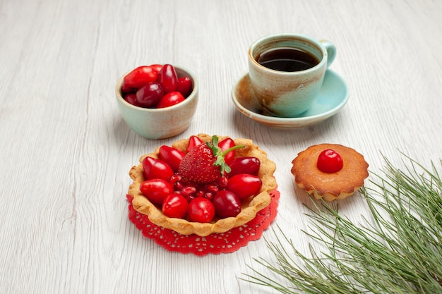 Vista frontale piccola torta con frutta e tazza di tè su scrivania bianca frutta dessert colore tè
