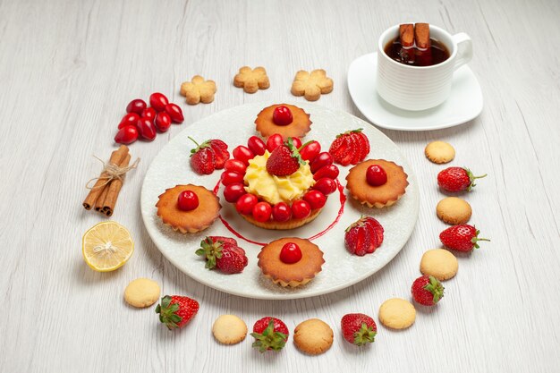 正面図白い机の上の果物とお茶の小さなケーキ果物のデザートケーキ
