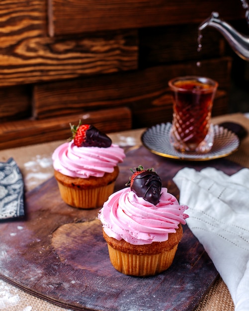 茶色の木製の机の上のピンクのクリームとチョコレートのストロベリーと正面の小さなケーキ