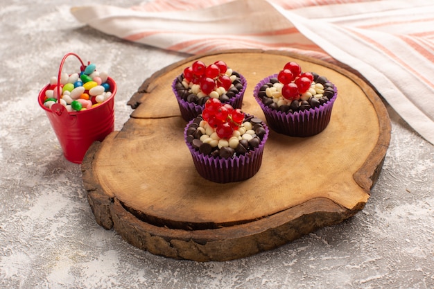 Бесплатное фото Вид спереди маленькие шоколадные пирожные с клюквой и конфетами на сером