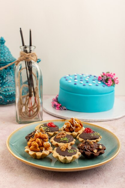 분홍색 책상 설탕 달콤한 케이크 생일 비스킷에 파란색 생일 케이크와 함께 접시 안에 전면보기 작은 초콜릿 케이크