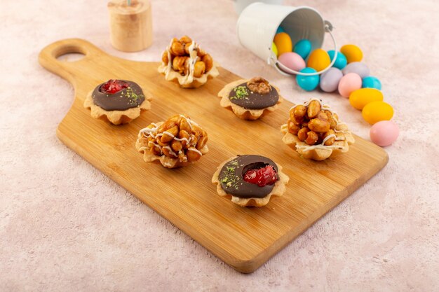 A front view little chocolate cakes with nuts and candies on the wooden desk sweet sugar color